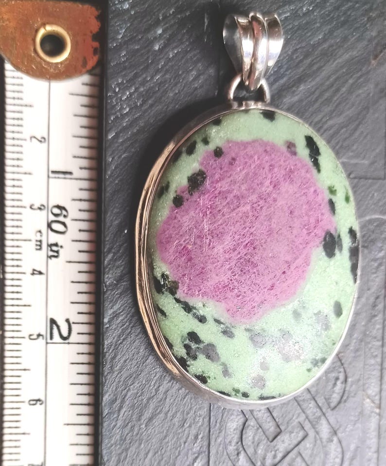 Pu&ograve; includere: Ciondolo ovale con anello argentato. Il ciondolo presenta una grande area rosa centrale circondata da pietra verde e macchiata di nero. Il ciondolo &egrave; lungo circa 5 cm.