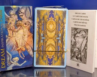 May include: A deck of "Dream Inspirational Cards" with a blue box featuring angel illustrations. The card deck has a gold and blue design with clock faces. A booklet with text in multiple languages is also included.