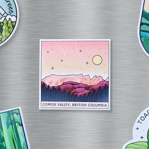 Peut inclure: Autocollant carré représentant un paysage stylisé avec des montagnes, des arbres et un coucher de soleil. Les couleurs sont le rose, le violet et le bleu. Le texte "COMOX VALLEY, BRITISH COLUMBIA" est en bas. Entouré d'autres autocollants.
