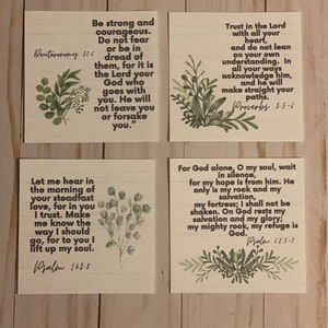 May include: Four wooden signs with inspirational quotes from the Bible. Each sign features a watercolor-style green leaf design. The quotes are: "Be strong and courageous. Do not fear or be in dread of them, for it is the Lord your God who goes with you. He will not leave you or forsake you." Deuteronomy 31:6, "Trust in the Lord with all your heart, and do not lean on your own understanding. In all your ways acknowledge him, and he will make straight your paths." Proverbs 3:5-6, "Let me hear in the morning of your steadfast love, for in you I trust. Make me know the way I should go, for to you I lift up my soul." Psalm 143:8, "For God alone, O my soul, wait in silence, for my hope is from him. He only is my rock and my salvation, my fortress; I shall not be shaken. On God rests my salvation and my glory; my mighty rock, my refuge is God." Psalm 62:5-7