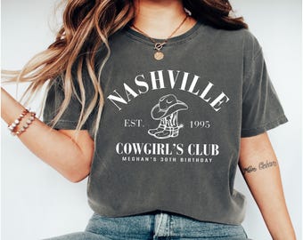 May include: Dark gray t-shirt with a white graphic that reads "Nashville Cowgirl's Club" with a cowboy hat and boots. The text "Est. 1995" and "Meghan's 30th Birthday" are also included in the design.