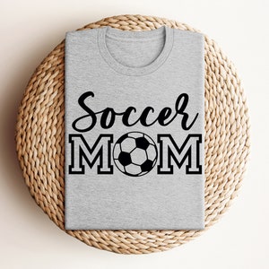 May include: Gray t-shirt with the text "Soccer Mom" in black lettering and a black and white soccer ball graphic.