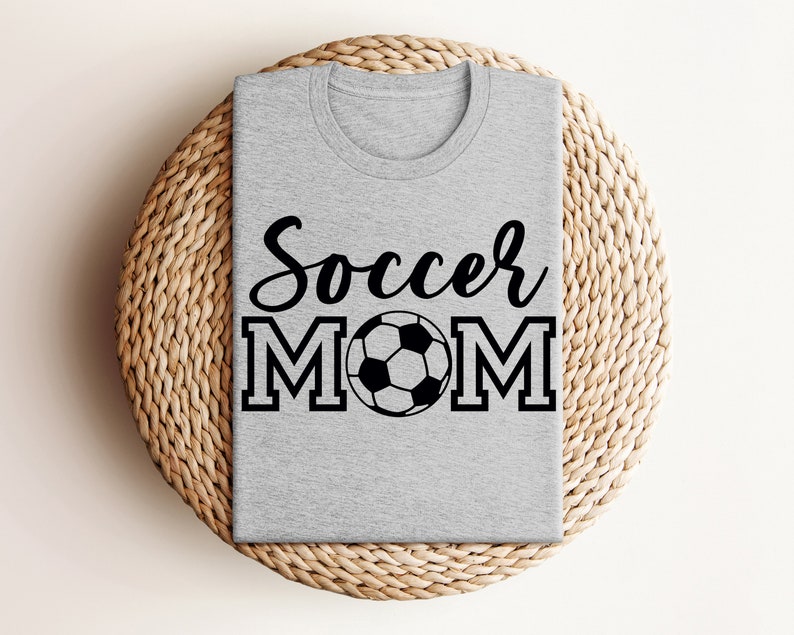 May include: Gray t-shirt with the text "Soccer Mom" in black lettering and a black and white soccer ball graphic.