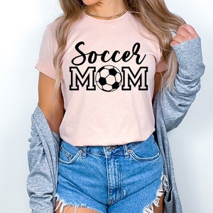 May include: A pink t-shirt with the text "Soccer Mom" in black lettering and a black and white soccer ball graphic.
