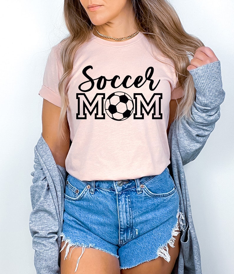 May include: A pink t-shirt with the text "Soccer Mom" in black lettering and a black and white soccer ball graphic.