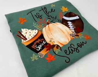 May include: Green fleece blanket with a fall-themed graphic. The design includes a pumpkin, a football, a pumpkin spice latte, and autumn leaves. Text reads "Tis the Season" in a script font.