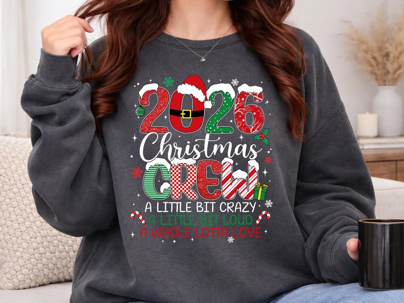 以下が含まれることがあります： 2026 CHRISTMAS CREW A LITTLE BIT CRAZY A LITTLE BIT LOUD A WHOLE LOTTA LOVEという文字がプリントされた、チャコールグレーのクルーネックトレーナー。赤と緑の模様、サンタの帽子、キャンディケインがデザインされています。