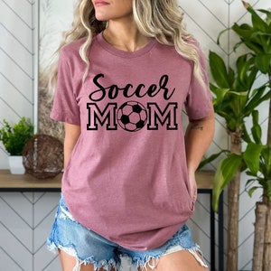 May include: A mauve t-shirt with the text "Soccer Mom" in black lettering with a black and white soccer ball in the middle of the word "Mom".
