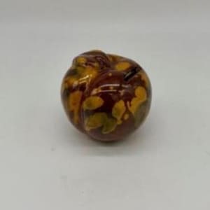 May include: A ceramic apple-shaped figurine with a glossy finish. The apple features a blend of brown, yellow, and green hues, with a detailed leaf pattern. The figurine is a decorative item.