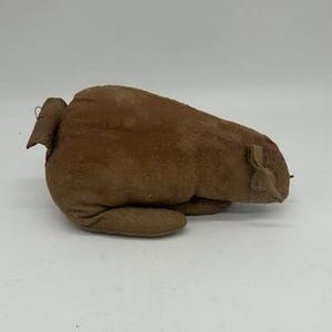 May include: A brown, plush, handmade stuffed animal shaped like a pig. The pig is lying on its belly with its head turned to the side.