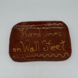 May include: A brown, rectangular ceramic tray with rounded edges. The tray features the text "Hard Times on Wall Street" in gold lettering, with decorative gold accents along the edges.