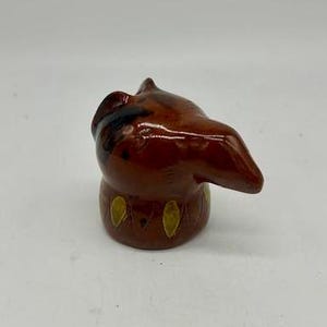 May include: A small ceramic figurine of a brown cat with gold accents. The cat is looking to the right and has its head tilted.