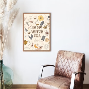 Könnte beinhalten: Ein gerahmter Druck mit beigem Hintergrund und verschiedenen skurrilen Illustrationen, darunter Sonne, Mond und Sterne. Der Text "IN MY WITCH ERA" ist mittig platziert. Der Rahmen ist braun.