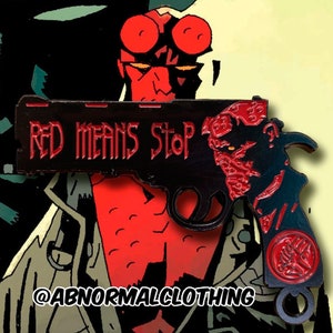 May include: Black and red enamel pin featuring a gun with the words "Red Means Stop" and a red devil head on the side. The pin is attached to a metal loop.