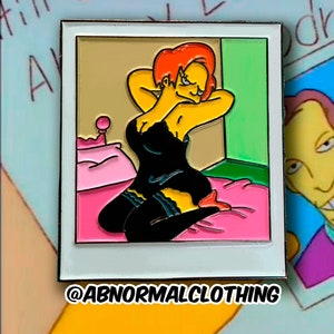 May include: A yellow cartoon character with red hair wearing a black dress and red heels. The character is sitting on a pink bed in a white frame with the text "@ABNORMALCLOTHING" below the frame.