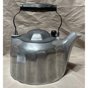 May include: A vintage aluminum tea kettle with a black wooden handle and lid knob. The kettle has a spout for pouring and a curved handle. The body of the kettle has vertical ridges. The kettle is designed for stovetop use.