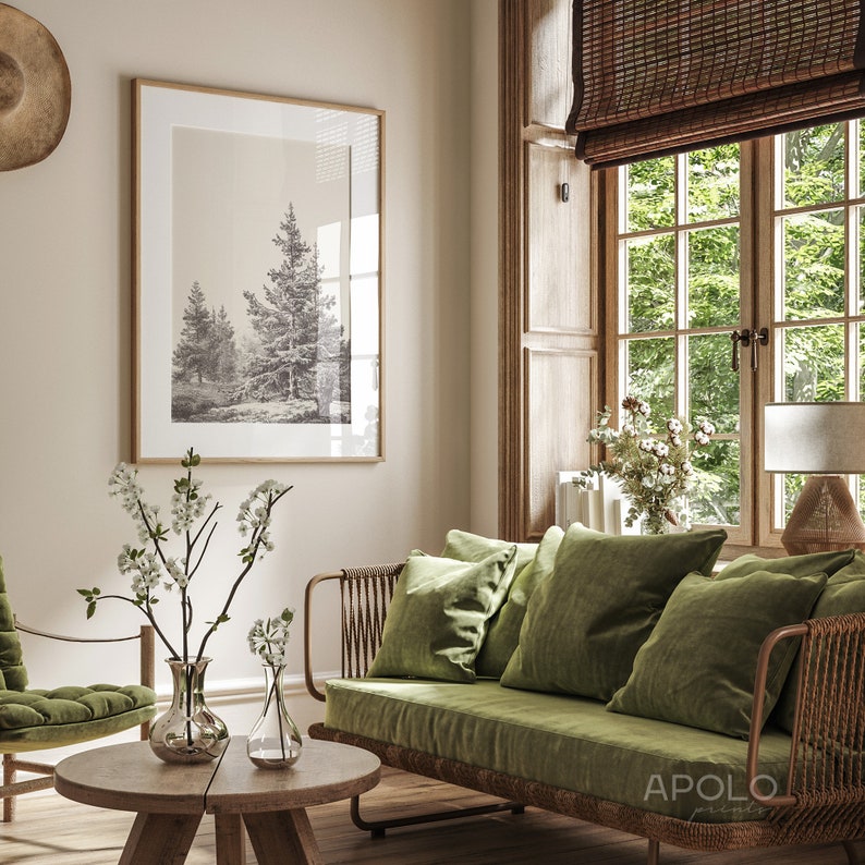 Op de afbeelding: Een groene fluwelen bank met een houten frame en geweven rotan details. De bank heeft drie kussens en staat in een woonkamer met een raam, een ingelijst afdruk van bomen en een vaas met witte bloemen op een houten salontafel.