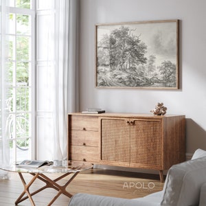 May include: A wooden cabinet with three drawers and two doors. The doors are made of woven rattan and have wooden knobs. The cabinet is sitting on a wooden floor in a living room with a white wall and a window with white curtains. A black and white framed print of a forest scene hangs on the wall above the cabinet. A glass coffee table with a wooden frame sits in front of the cabinet.