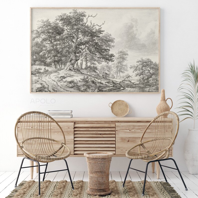 May include: A black and white sketch of a woodland scene with trees and a path. The sketch is framed and hanging on a white wall above a wooden cabinet with two wicker chairs and a small wicker stool.