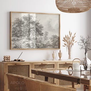 May include: A black and white drawing of a woodland scene hangs above a wooden cabinet with woven rattan doors. The cabinet is topped with a glass vase filled with dried grasses, two decorative ceramic vases, and a glass teapot.