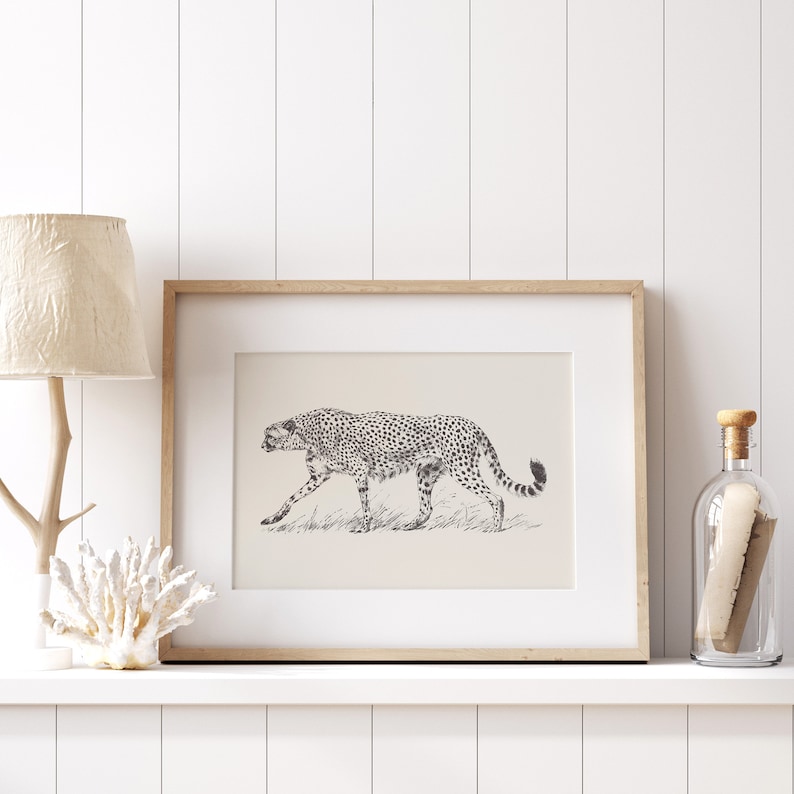 May include: A framed black and white illustration of a cheetah walking through tall grass. The frame is made of light wood and has a white mat.