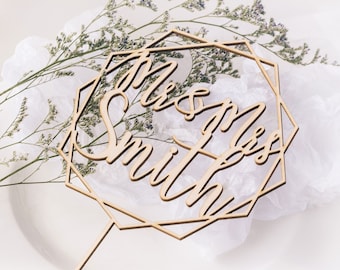 Könnte beinhalten: Holz-Kuchentopper mit geometrischem Design und dem Text "Mr & Mrs Smith" in kursiv.