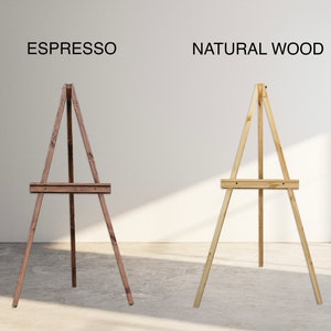 Pu&ograve; includere: Due cavalletti in legno, uno in marrone espresso e uno in legno naturale, in piedi su un pavimento grigio chiaro. I cavalletti sono entrambi in legno e hanno un design semplice.