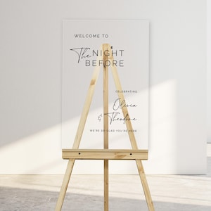 Pu&ograve; includere: Un cartello in acrilico trasparente su un cavalletto con il testo "Welcome to The Night Before Celebrating Olivia & Theodore We're so glad you're here."