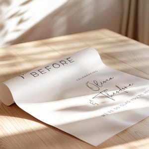 Pu&ograve; includere: Un cartello bianco con il testo "Before Celebrating Olivia & Theodore We're so glad you're here" in corsivo nero.