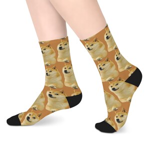 May include: Crew socks with a repeating pattern of Shiba Inu dog faces. The socks have a brown background, with black heels and toes. The socks are designed to be worn on the feet.