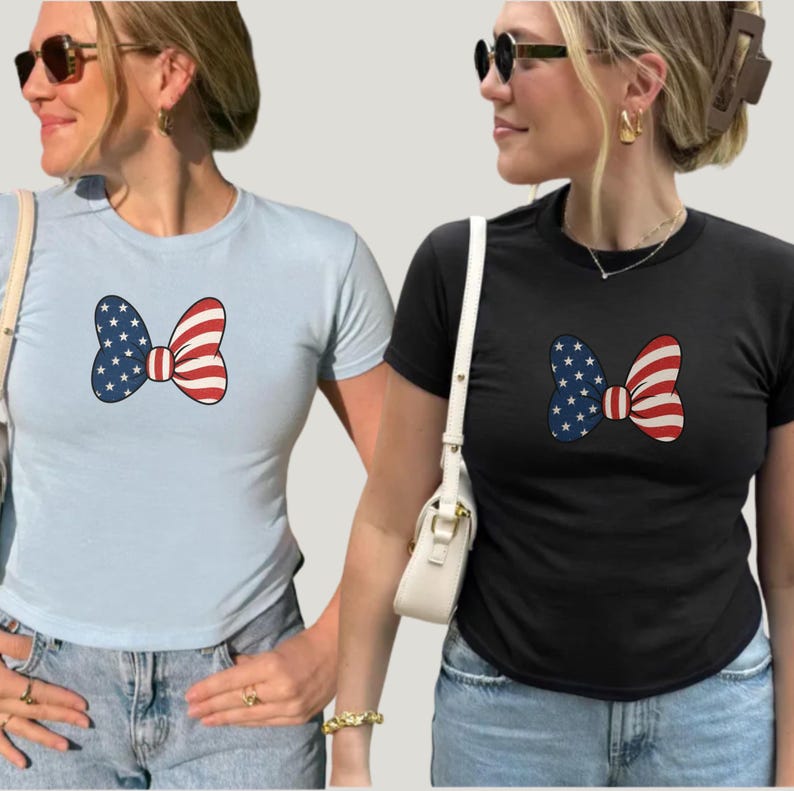 May include: Two short-sleeved t-shirts, one light blue and one black, each featuring a bow design. The bow design incorporates the American flag with blue stars and red and white stripes, creating a patriotic theme.