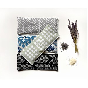 May include: Four rectangular aromatherapy pillows with patterned fabric in gray, blue, and black. A bundle of dried lavender, lavender buds, and rice are also displayed. The pillows are designed for relaxation and wellness.
