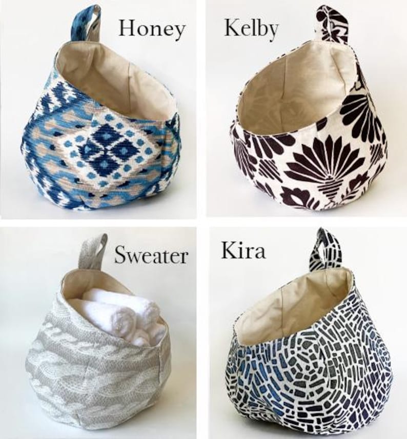 Puede incluir: Cuatro cestas de almacenamiento de tela colgantes con diferentes patrones. Las cestas est&aacute;n etiquetadas como "Honey", "Kelby", "Sweater" y "Kira".