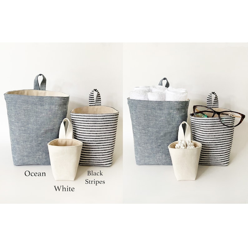 May include: Three hanging fabric storage baskets in ocean blue, black and white stripes, and white. The ocean blue basket holds rolled towels. The black and white striped basket holds eyeglasses. The white basket is small and holds cotton swabs.