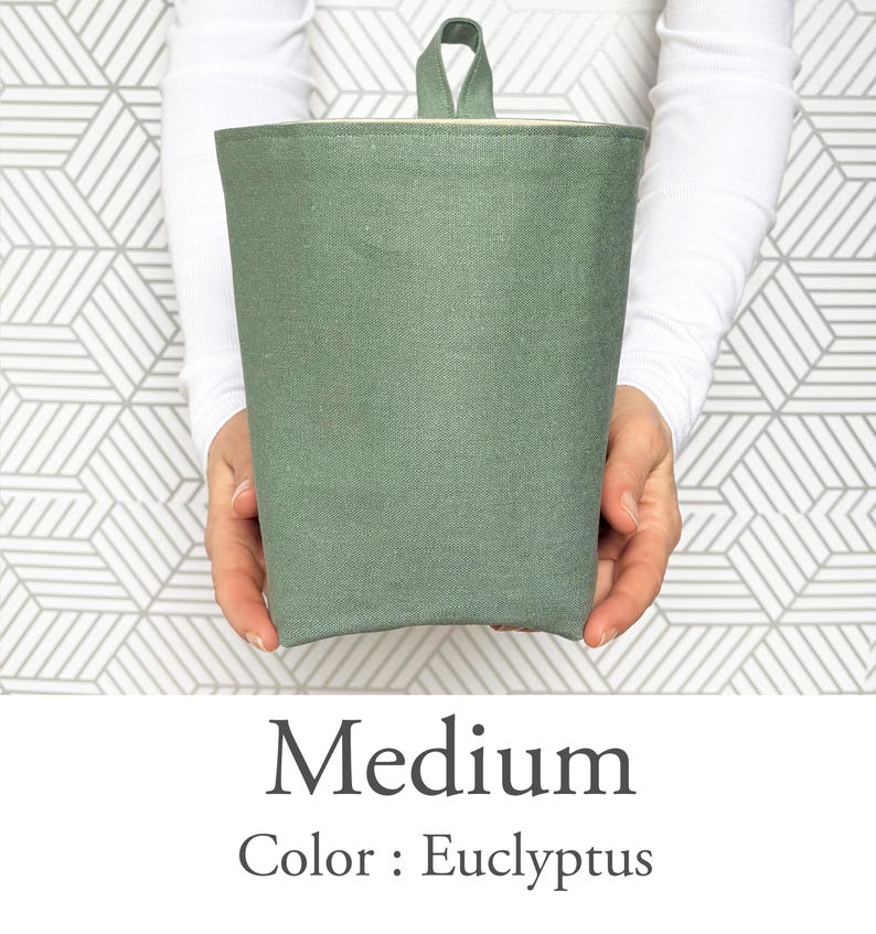 May include: A medium-sized, eucalyptus-colored fabric container with a loop handle. The container is cylindrical with a folded top edge and a light-colored interior. The text "Medium" and "Color: Eucalyptus" are displayed below the container.