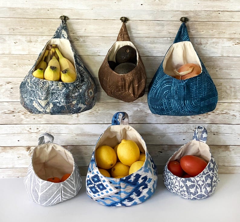 Puede incluir: Seis cestas de almacenamiento de tela colgantes con diferentes patrones y colores. Las cestas est&aacute;n llenas de varias frutas y verduras, incluyendo pl&aacute;tanos, limones, limas, aguacates y tomates.