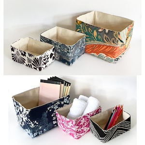 May include: A collection of fabric storage bins in various sizes and patterns. The bins feature floral, geometric, and abstract designs in colors like brown, blue, pink, and orange. Some bins contain items such as notepads, pencils, and towels.