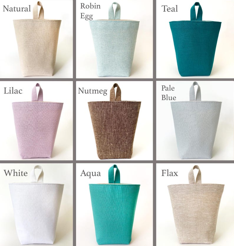 May include: Nine fabric doorstops in various colors, including natural, robin egg, teal, lilac, nutmeg, pale blue, white, aqua, and flax. Each doorstop has a trapezoidal shape with a small loop handle at the top.