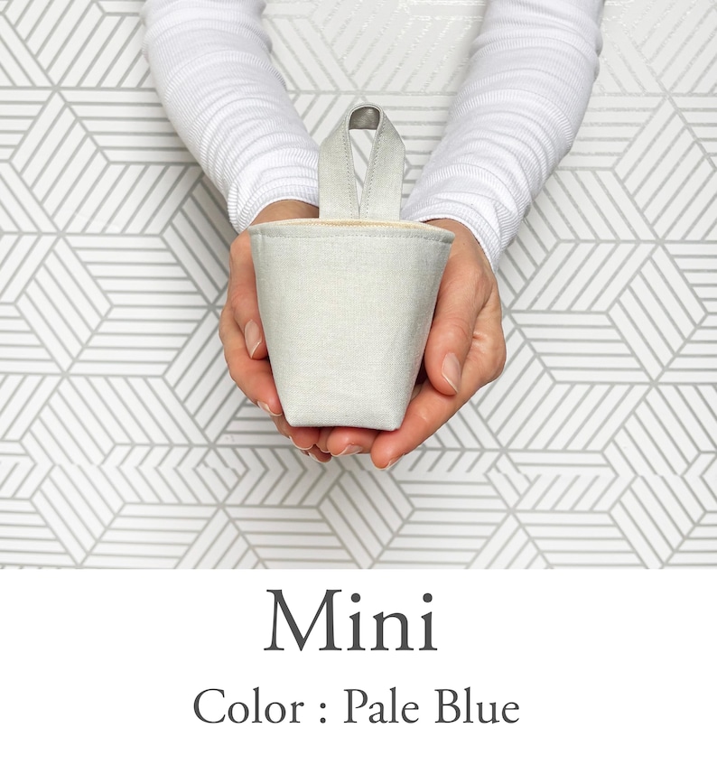 May include: A pale blue mini bucket-shaped container with a handle, held in two hands. The container is made of a textured fabric. The text "Mini" and "Color: Pale Blue" are below the container.