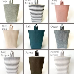May include: Nine fabric storage bins in various colors and patterns. Colors include sage, black stripes, dusty pink, pale pink, rain, ocean, gray stripes, forest, and natural stripes. Each bin has a matching handle.