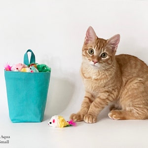 May include: A small, aqua-colored cat toy storage bin with a handle, filled with colorful toy mice. A ginger tabby cat sits beside the bin, with a toy mouse in front of it. The text on the image reads "Color: Aqua Size: Small."