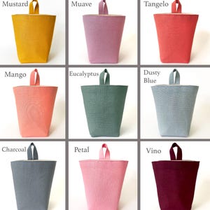 May include: A collection of fabric storage bins in various colors, including mustard, mauve, tangelo, mango, eucalyptus, dusty blue, charcoal, petal, and vino. Each bin has a handle and a contrasting interior.