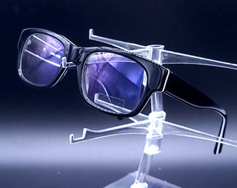May include: Black framed glasses with blue tinted lenses on a clear plastic display stand.