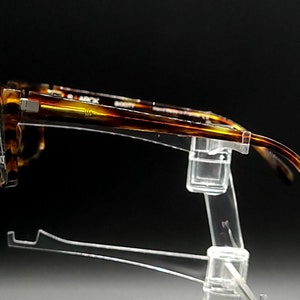 Puede incluir: Gafas de pasta de carey en un expositor de pl&aacute;stico transparente. Las gafas son de color marr&oacute;n y dorado.