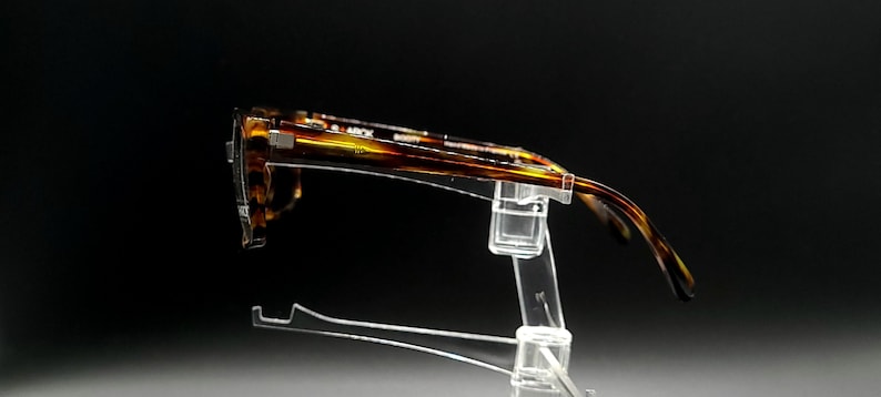 Puede incluir: Gafas de pasta de carey en un expositor de pl&aacute;stico transparente. Las gafas son de color marr&oacute;n y dorado.