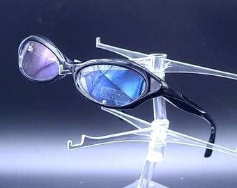 May include: Black sunglasses with a blue and purple mirrored lens. The sunglasses are on a clear plastic display stand.