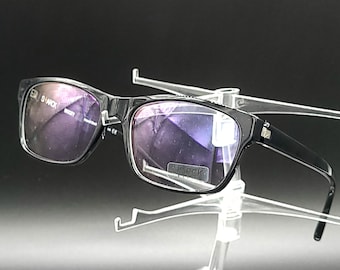May include: Black rectangular eyeglasses with a clear frame and purple tinted lenses. The glasses are on a clear plastic stand.