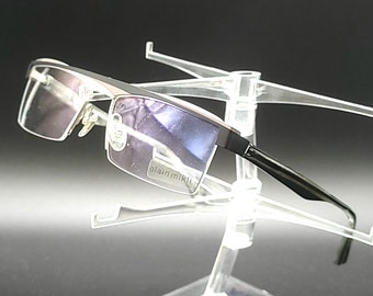 May include: Silver and black rectangular frame eyeglasses with clear lenses. The glasses are on a clear plastic display stand.