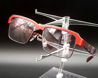 May include: Red and black framed eyeglasses with a clear plastic display stand.