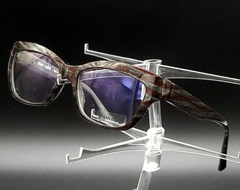 May include: A pair of eyeglasses with a camouflage pattern frame and purple tinted lenses. The glasses are on a clear plastic display stand.